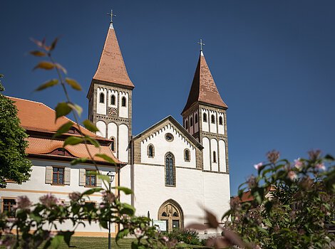 Das Kloster mit seinen zwei Türmen inmitten grüner Büsche. Der Himmel strahlt wolkenlos.