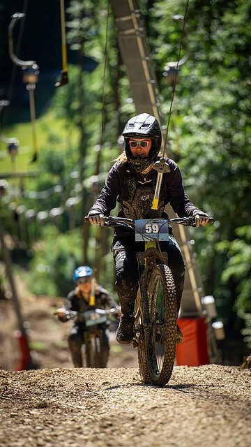 Ein Schlepplift, der an den Lenker angehängt ist, zieht zwei Mountainbiker durch den Wald bergauf.