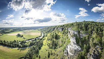 Weiter Blick ins Altmühltal: Rechts Felsen mit grünem Hang ins Tal  und rechts sieht man den Fluss im Tal mit Wiesen.