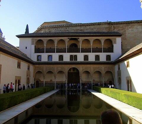 Innenhof mit rechteckigem Wasserbecken, umgeben von historischen Gebäuden mit Arkaden und verzierten Fassaden.