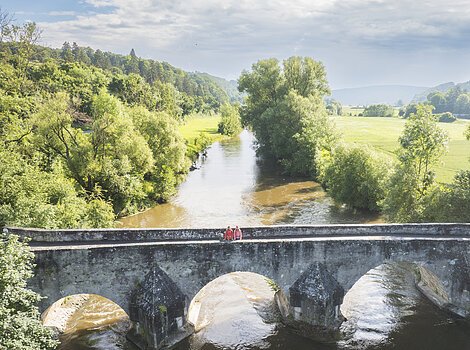 Eine alte, massige steinerne Brücke überspannt den Fluss und der Blick geht weit ins grüne Altmühltal.
