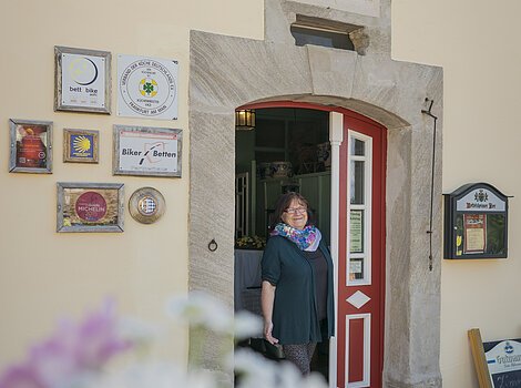 Eine Frau steht in der offenen Tür eines Gebäudes mit mehreren Schildern an der Wand.