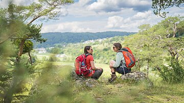 Zwei Frauen mit Rucksack sitzen auf Felsen am Talhang und sprechen miteinander
