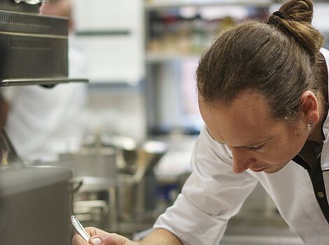 Ein Koch in einer Küche verfeinert ein Fischgericht auf einem Teller mit einer Soße.