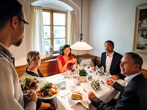 Eine Gruppe von vier Personen sitzt an einem gedeckten Tisch in einem Restaurant, während ein Kellner Essen serviert.