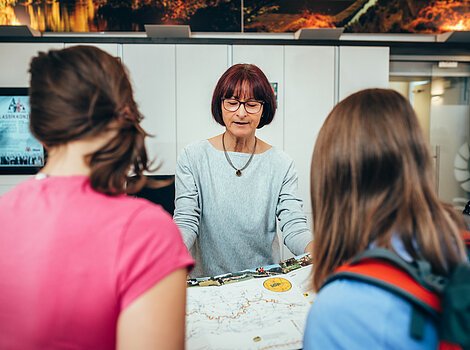 Frau zeigt zwei Personen eine Landkarte in einem Informationsbüro.
