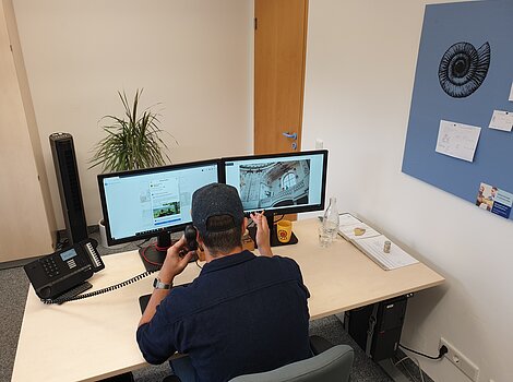 Werkstudent im Naturpark Altmühltal Person mit Baseballkappe sitzt an Schreibtisch mit zwei Monitoren und telefoniert im Büro.