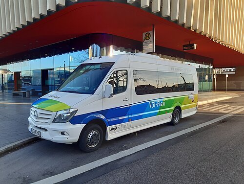 VGI Flexi Bus Der VGI Flexi Bus, ein Kleinbus, parkt vor dem Nordbahnhof in Ingolstadt. Der Eingangsbereich mit der roten Fassade ist im Hintergrund zu erkennen.