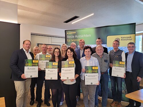 Gruppenfoto von zwölf Personen, einige halten Urkunden, im Hintergrund ein Banner mit dem Text „Beste Aussichten für Wanderer“ und „Naturpark Altmühltal“.